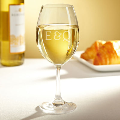 Wine glass filled with white wine on a table, with a blurred bottle and croissants in the background.