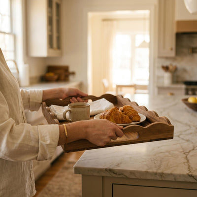 Person carrying a wood scalloped serving tray with coffee and croissants