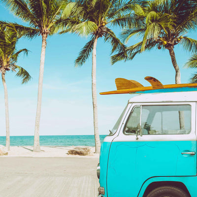 Retro beach van parked near palm trees and the ocean under a bright blue sky