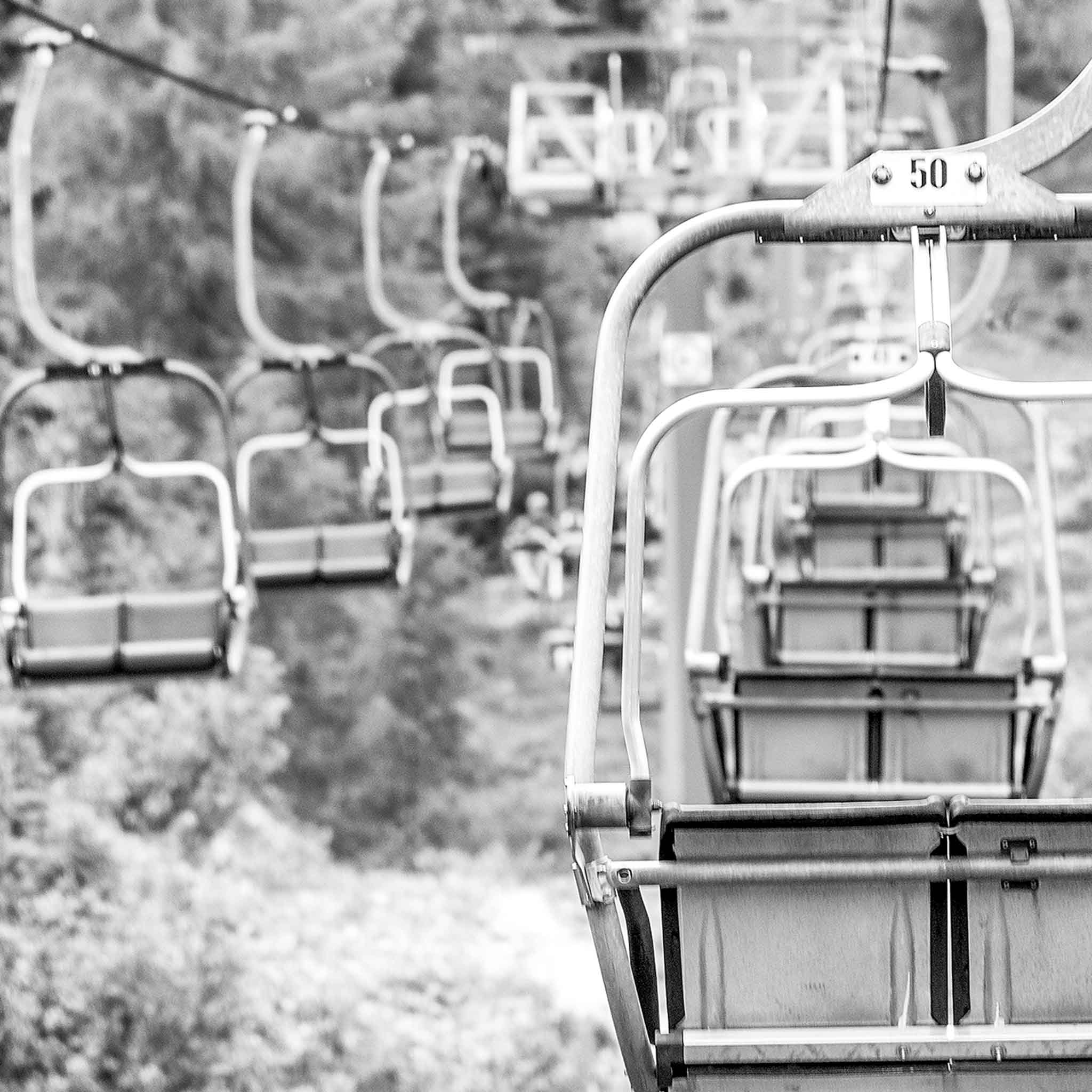 Empty chairlift seats travel over a wooded slope
