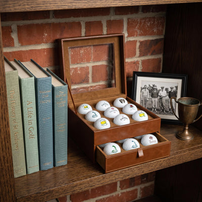 Open golf ball display case arranged on a wooden bookshelf