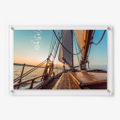 Acrylic wall art featuring the wooden deck and raised sails of a classic sailboat at sunset