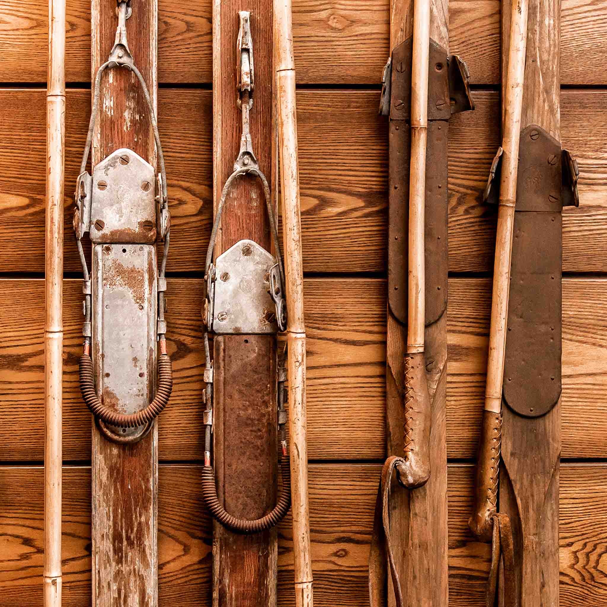 Antique skis and ski poles arranged on a wooden lodge wall in warm brown tones