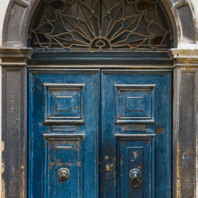 Vintage blue double door with worn paint, carved panels, and metal ring knockers