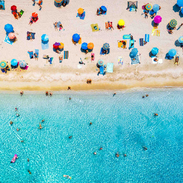 Aerial beach view showing bright umbrellas, sunbathers, and swimmers along the shoreline