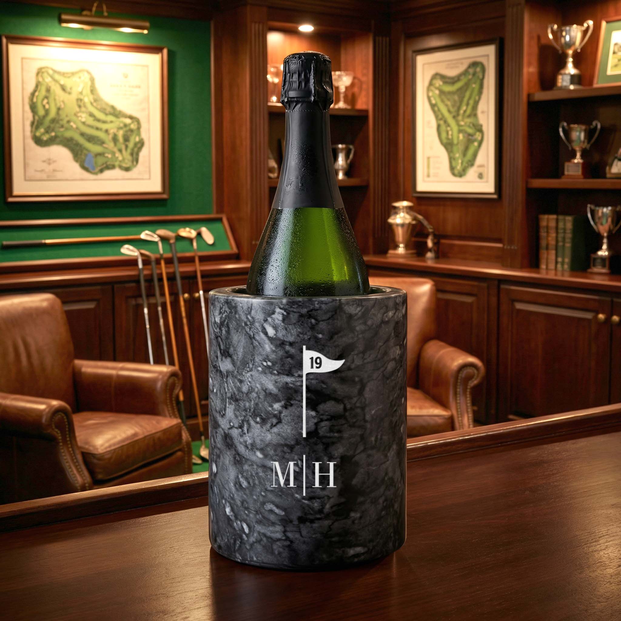 Bottle of champagne in a marble cooler with initials in a room with trophies and maps on the wall.
