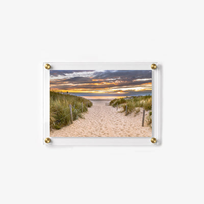 Scenic dune path leading to the sea as warm sunlight glows beneath layered clouds