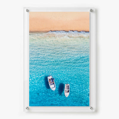 Acrylic wall art featuring two small boats floating in clear turquoise water near a sandy beach