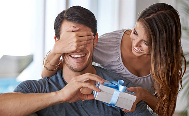 woman surprising man with gift by putting hand over eyes