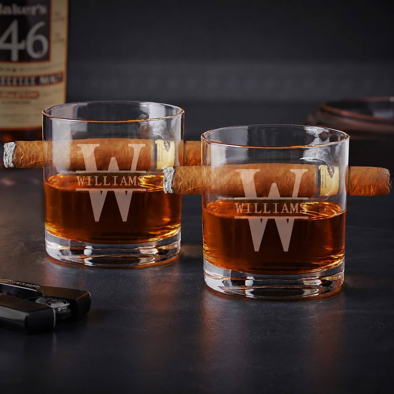 Two glasses of whiskey with a cigar on a dark surface.