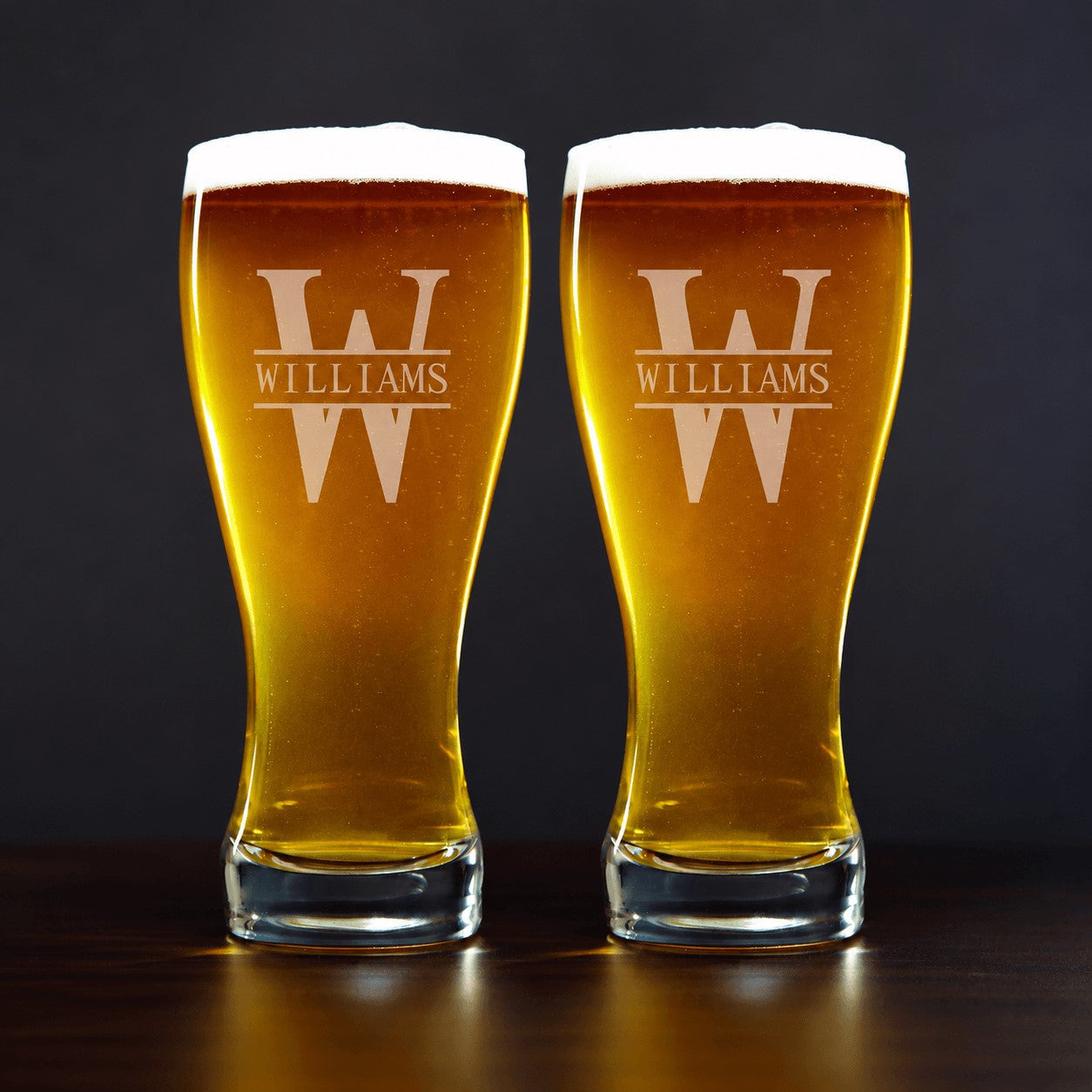 Two glasses of beer with 'Williams' engraving on a dark background