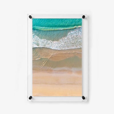 Vertical coastal wall art showing gentle surf meeting a smooth shoreline from above