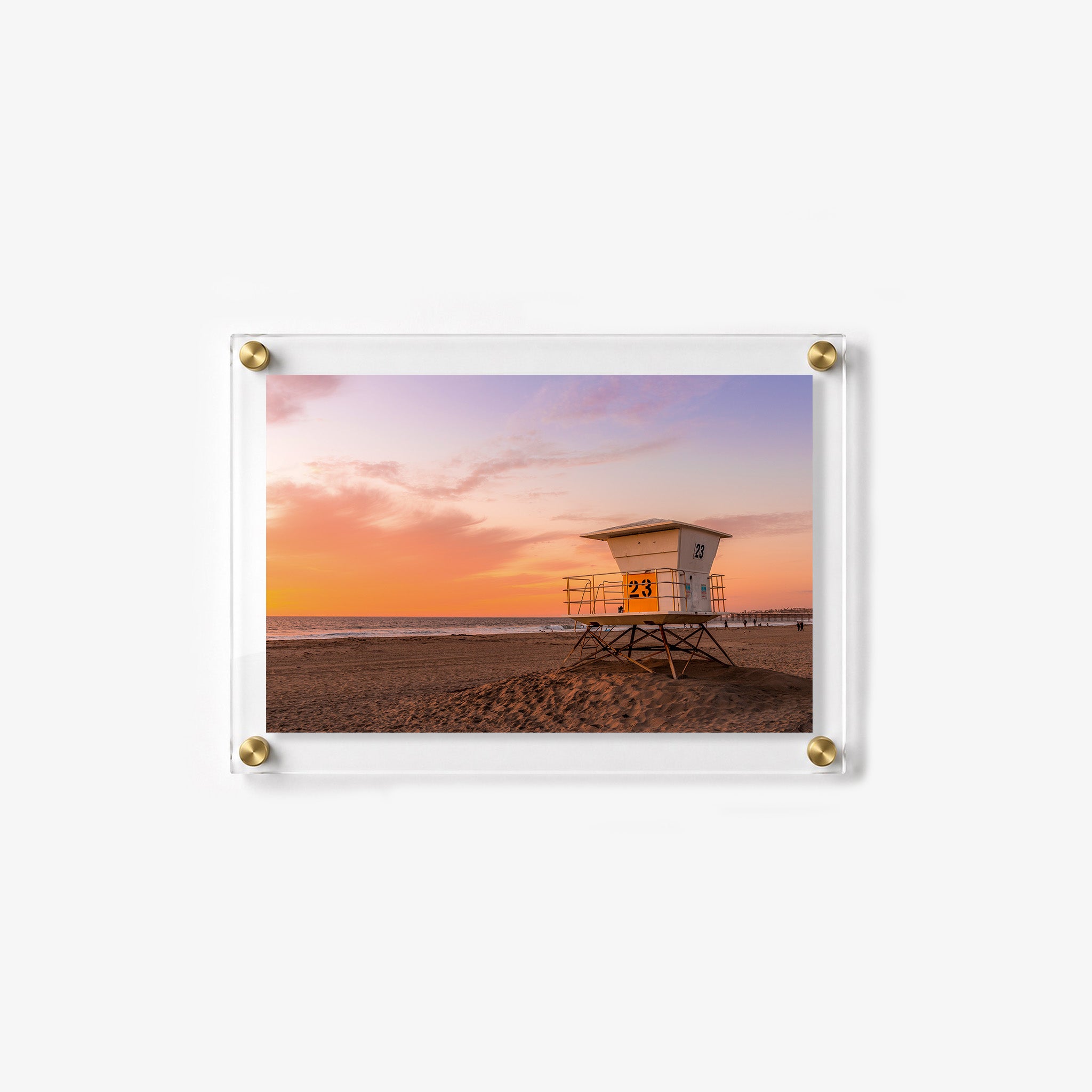 Lifeguard tower standing on a quiet beach as the sky turns orange, pink, and lavender