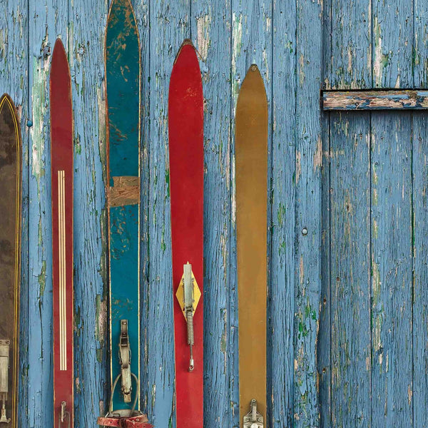 Colorful vintage skis leaning against a rustic blue wood wall