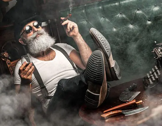 Bearded man smoking cigars and drinking whiskey