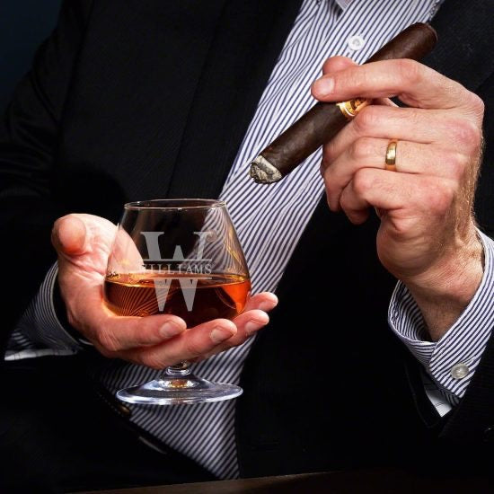 Man in suit swirling cognac glass while smoking cigar