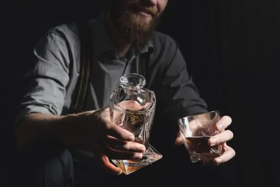 Bearded man holding a whiskey decanter and glass