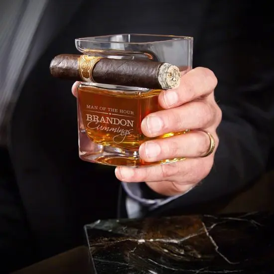 Man holding a cigar glass with a lit cigar attached