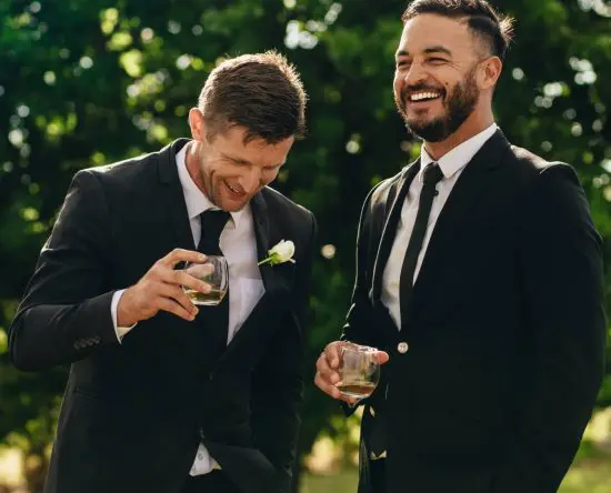 Groom and groomsman smiling and holding drinks