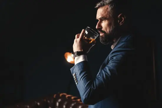 Man in suit with a beard drinking whiskey