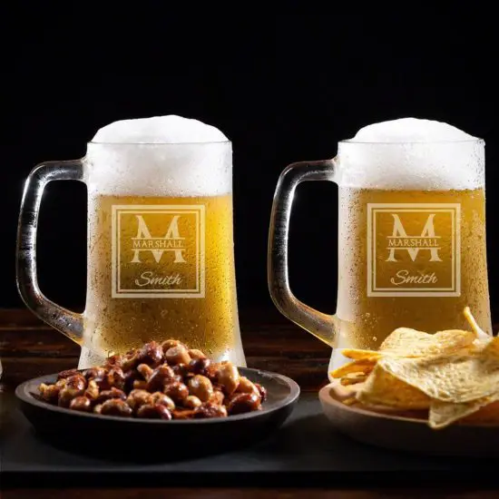 Two full beer mugs with nuts and chips in front