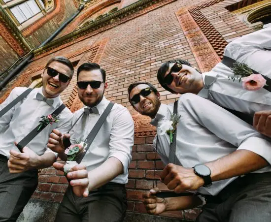 Four groomsman and groom posing near brick wall