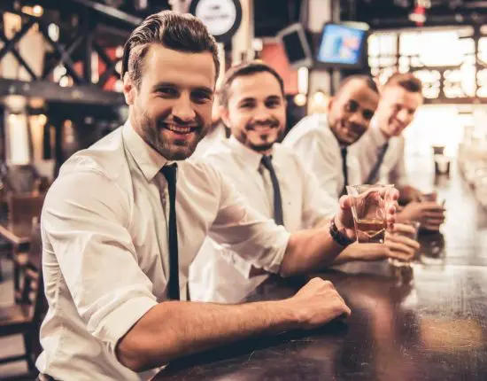 Four men at a bar enjoying whiskey