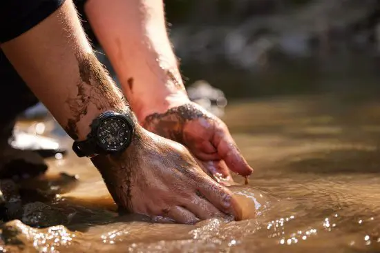 Man wearing Garmin smartwatch with hands in mud