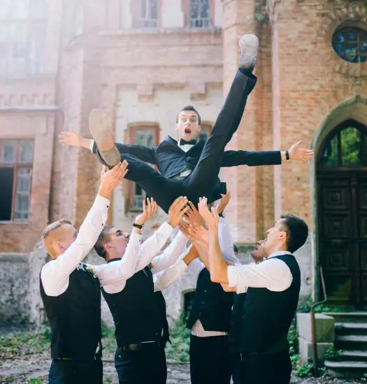 Four groomsmen throwing groom into the air