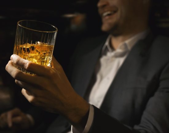 Man in suit laughing and drinking bourbon