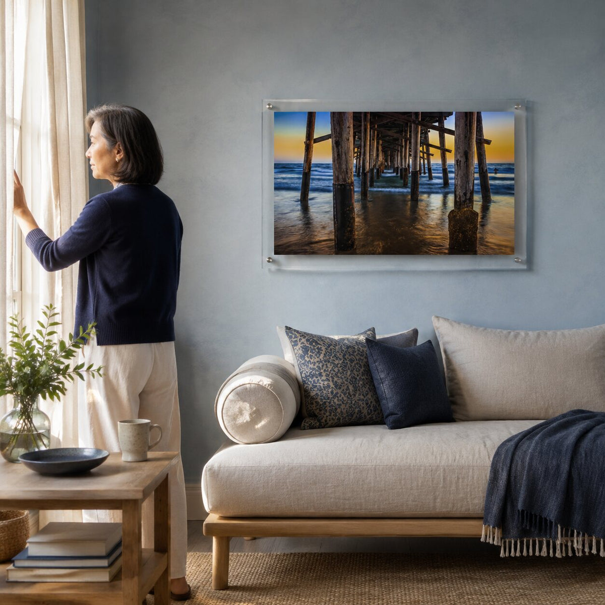 Pier Pressure acrylic wall art displayed above a modern living room sofa with woman standing
