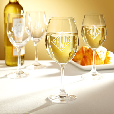 Three wine glasses with white wine on a table, a wine bottle in back, and croissants on a plate.