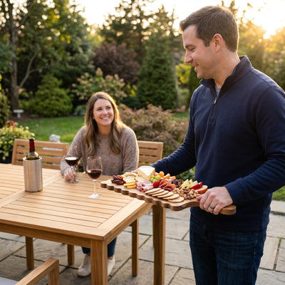 Man bringing a loaded scalloped acacia cheese board to a patio table