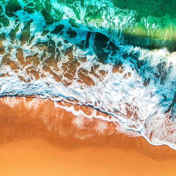 Aerial beach view showing white seafoam rolling across a copper colored shoreline