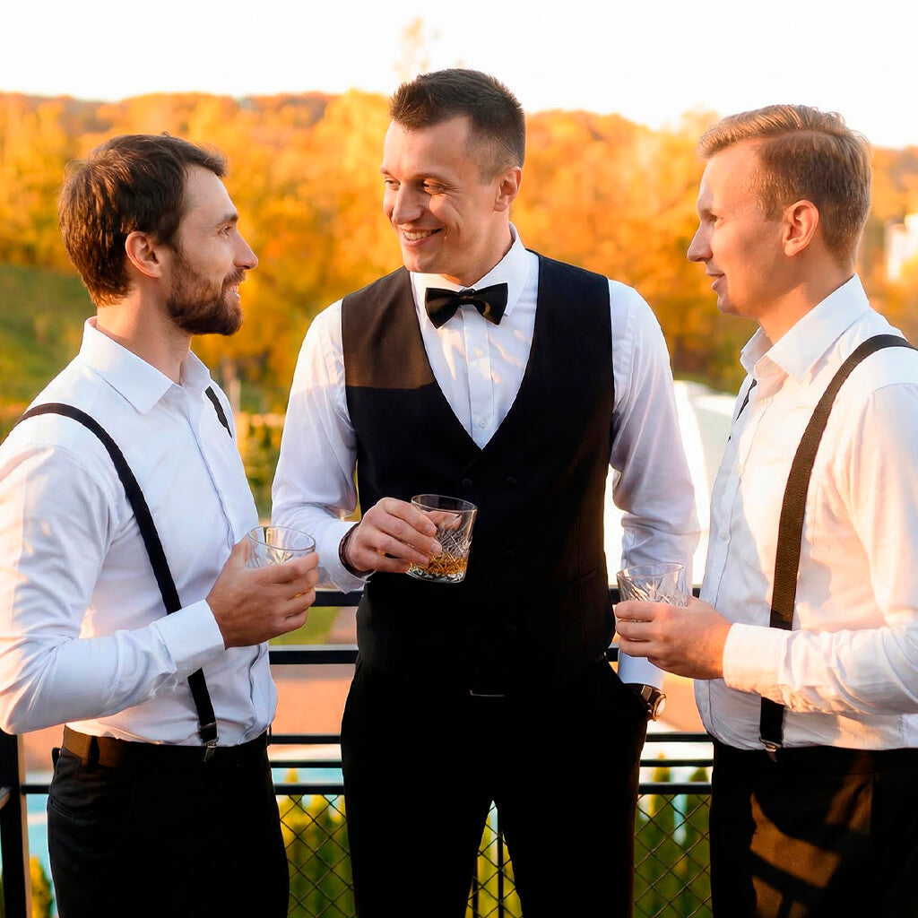 Three men in formal attire with suspenders standing outdoors against a blurred natural background
