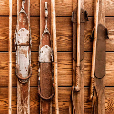 Antique skis and ski poles arranged on a wooden lodge wall in warm brown tones