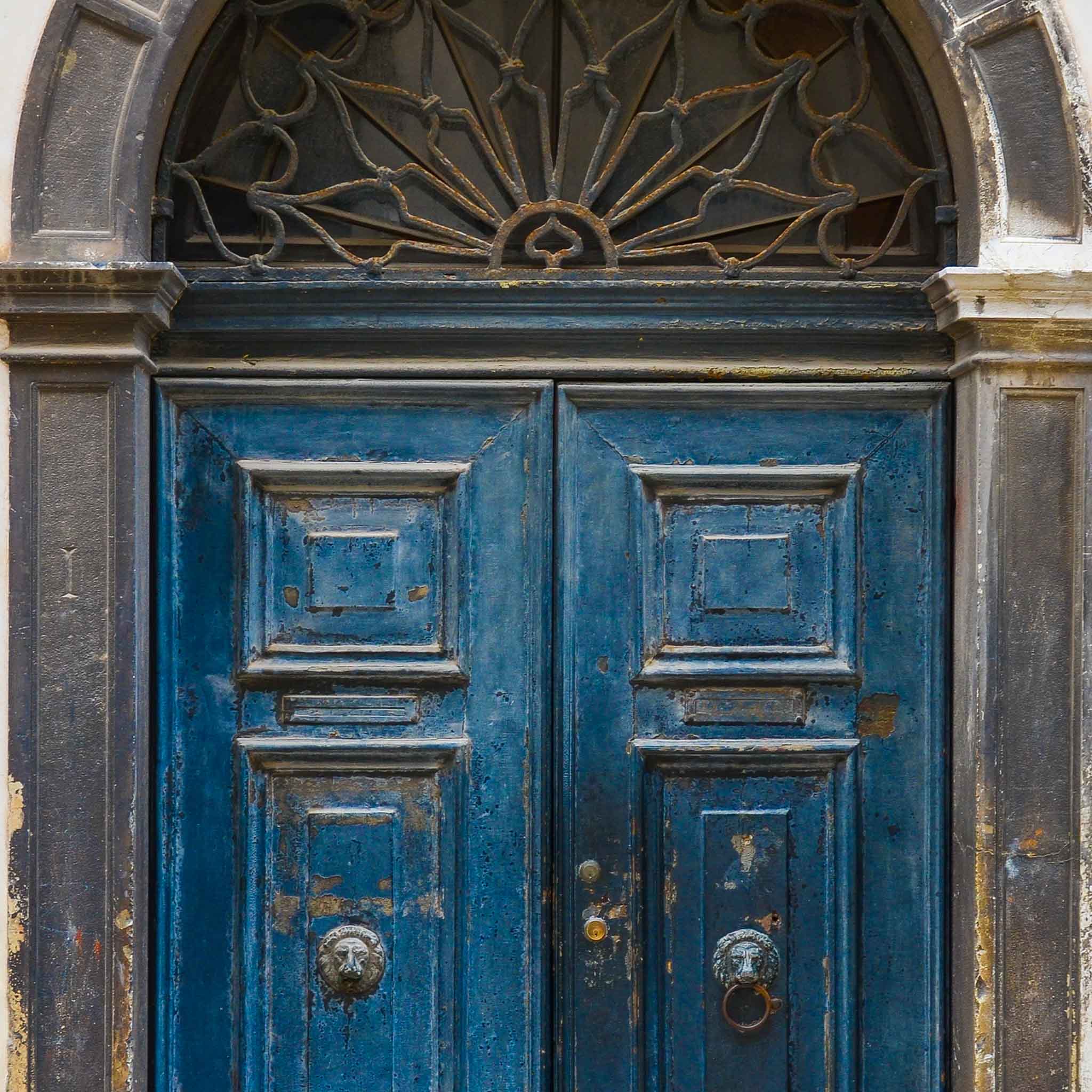 Vintage blue double door with worn paint, carved panels, and metal ring knockers