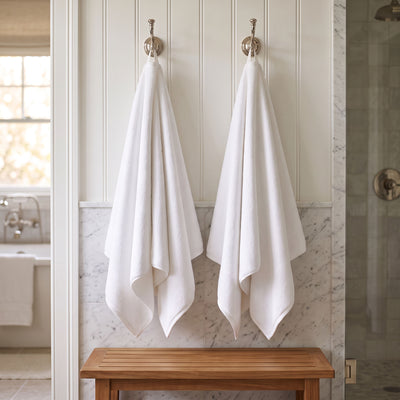 Two plush white Turkish cotton bath towels hanging from silver hooks