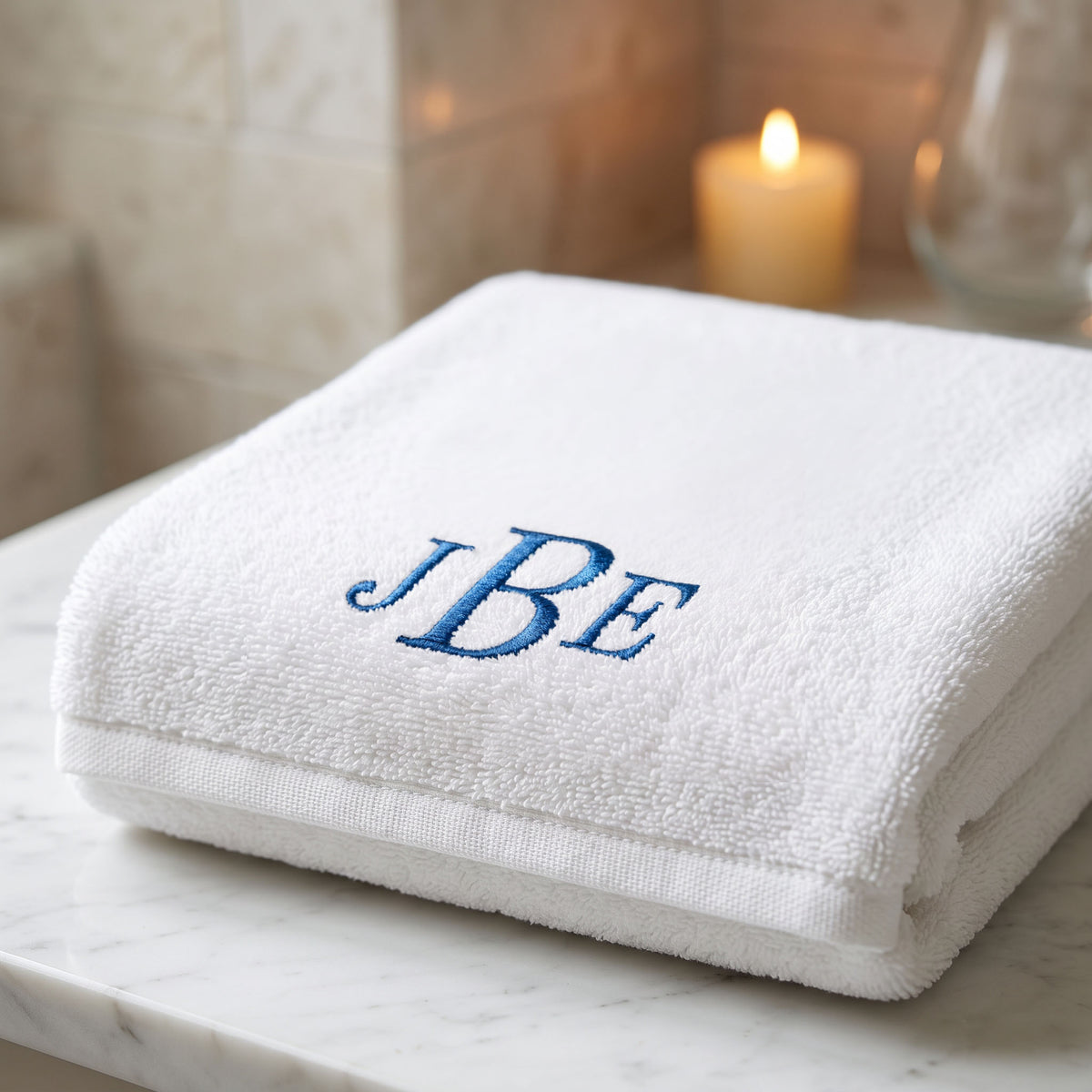 Folded plush white Turkish cotton towel with blue JBE embroidered initials