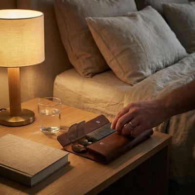 Person opening leather weekly pill case on a bedside table