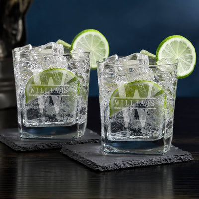 Two glasses with ice and lime wedges on dark coasters against a dark background
