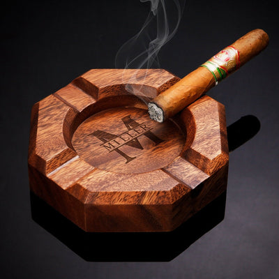 Lit cigar resting on an octagonal wooden ashtray with “MILLER” engraved, smoke rising against a dark background.
