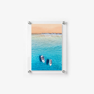 Two boats rest in shallow blue water as waves roll toward the shore