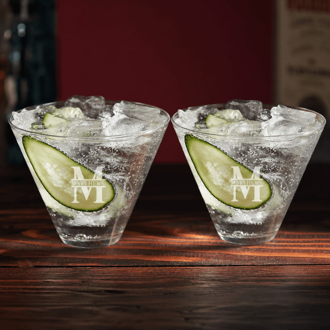 Two cocktails with lime slices and ice in martini glasses on a wooden surface.