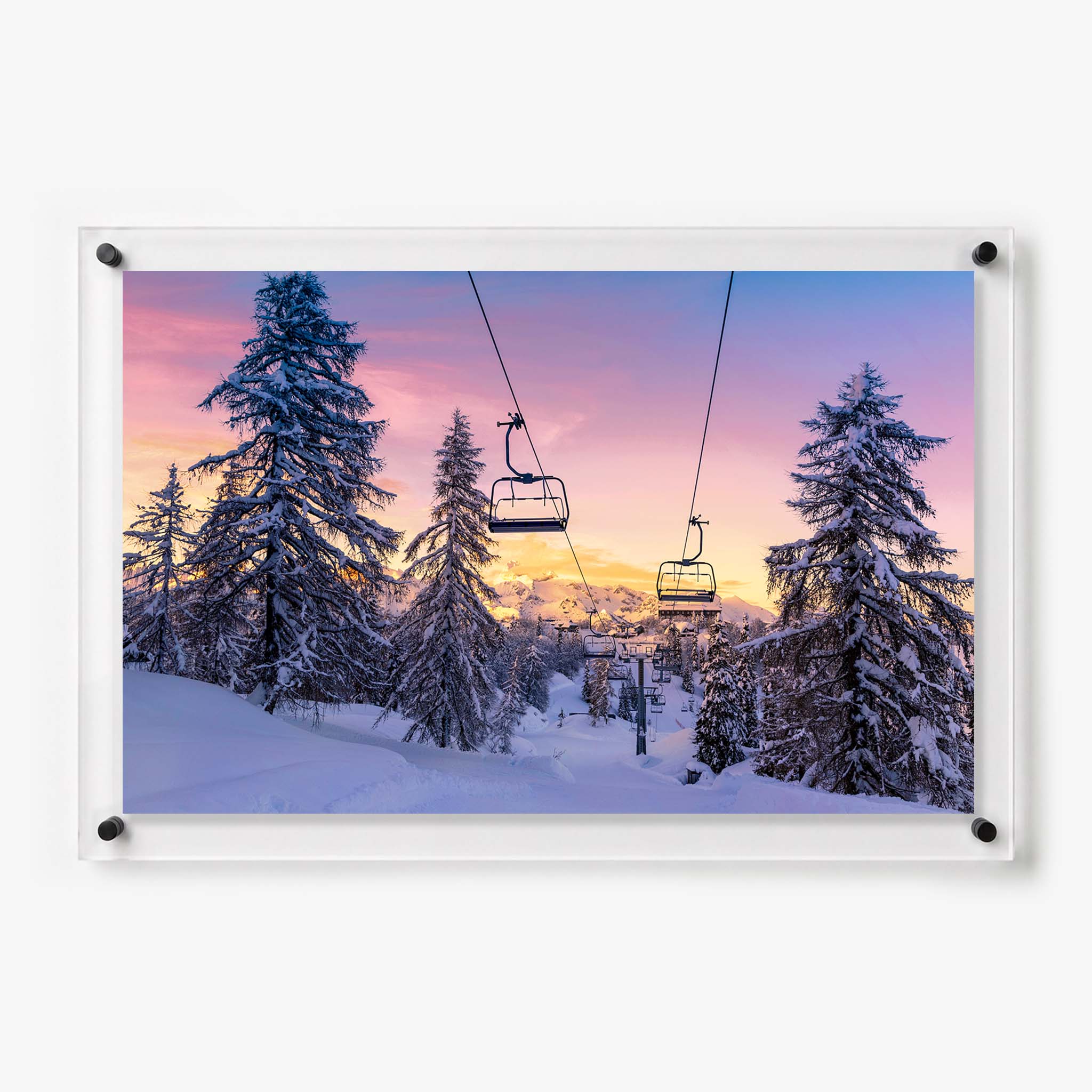 Snow covered pine trees and empty ski lifts beneath a pink and golden sunset sky