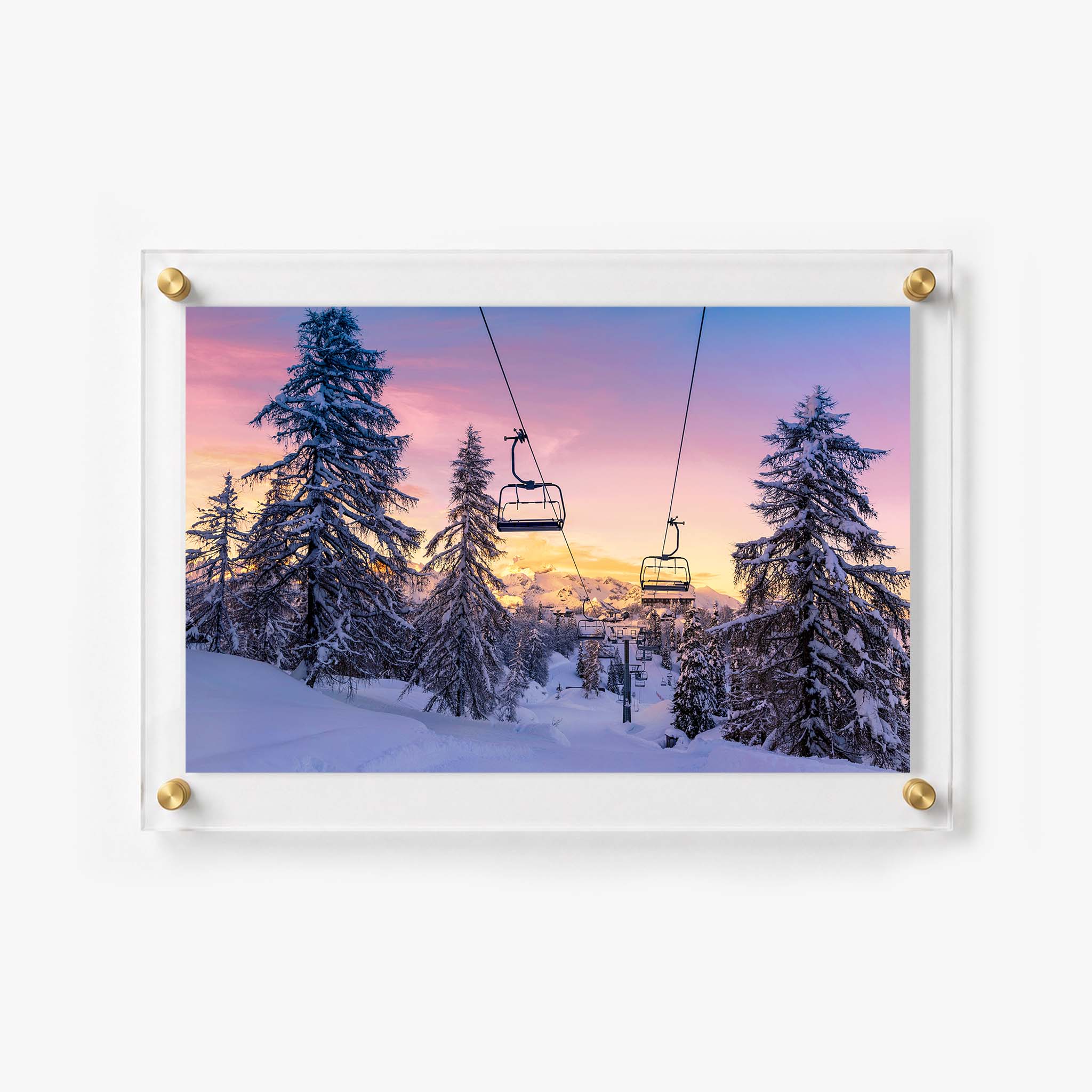 Empty chairlifts crossing a snow filled alpine landscape under soft pink clouds