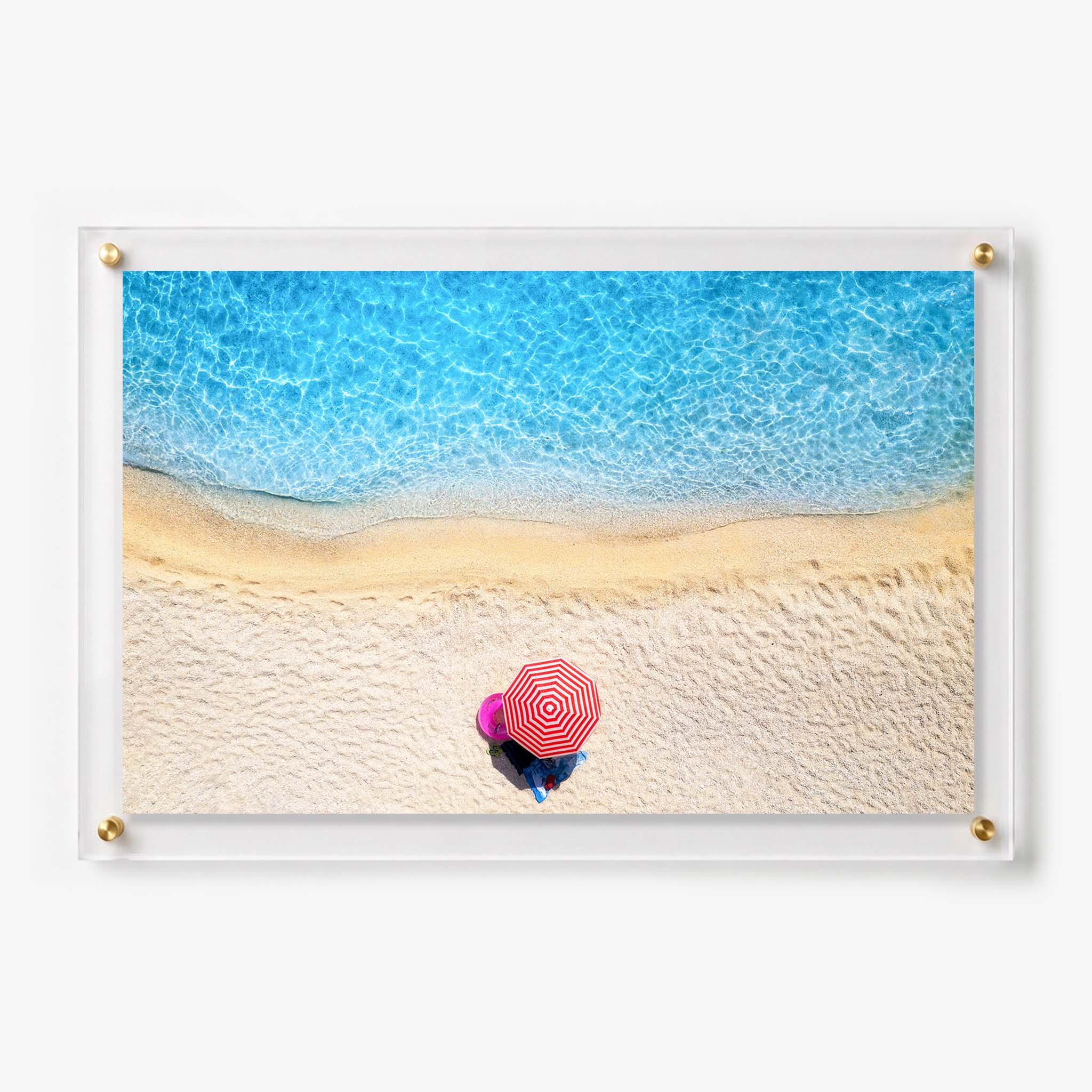 Aerial beach view with a red and white striped umbrella beside clear blue water