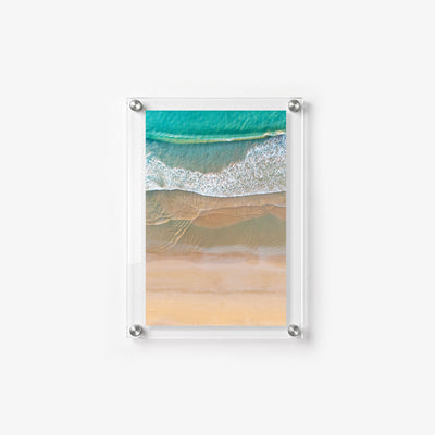 Aerial beach scene with turquoise water, foamy waves, and layered bands of wet sand