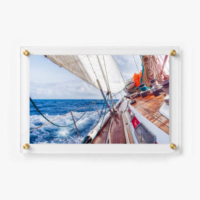 Sailboat deck with polished wood, coiled ropes, white sails, and foaming ocean water